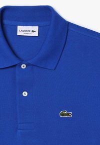 Modrá polo košeľa Lacoste s rebrovaným golierom, dvoma bielymi gombíkmi a malým vyšívaným logom krokodíla na ľavej hrudi. Textúrovaná tkanina.