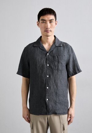 Chemise en lin gris anthracite à manches courtes avec un col, une poche avant et des boutons blancs. Elle présente une coupe décontractée et une texture légère.