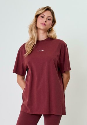 Burgundijas krāsas pārslodzes t-krekls, izgatavots no mīksta kokvilnas, ar īsām piedurknēm un apaļu kakla izgriezumu, uz krūtīm ir neliels balts logotips.