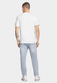 Biała bawełniana koszulka z krótkim rękawem, widok z tyłu. Połączona z jasnoniebieskimi dżinsami i białymi trampkami, charakteryzującymi się swobodnym krojem.