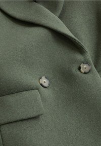 Tissu de manteau en laine vert foncé avec deux grands boutons ronds et une poche à rabat visible à l'avant.