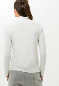 Weißes Langarmoberteil mit weicher, glatter Textur und leichtem Stehkragen, kombiniert mit grauen Hose mit elastischem Bund.