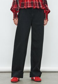 Pantaloni larghi in denim nero con vita alta e risvolti, abbinati a scarpe rosse con dettagli bianchi. Tessuto strutturato e vestibilità rilassata.