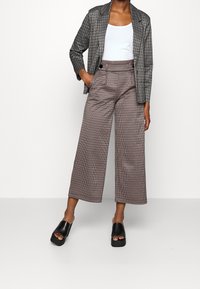 Rutig blazer i svart och grått, matchad med houndstooth-höga vida byxor. Bärs med svarta plattformssandaler.