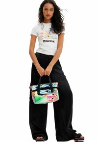 Bunt bedrucktes grafik t-shirt, schwarze weite hosen und eine lebhafte gemusterte tasche mit oberen traggriffen. Glattes material mit verspielten designelementen.