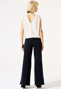 Ivoor gebreide top met V-rug en knoopdetails, gecombineerd met hoge zwarte wijde jeans. Glad textuur, casual pasvorm en strakke lijnen.