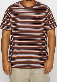Camiseta de rayas marrón y naranja hecha de algodón con cuello redondo. Presenta un pequeño logo rojo de Levi's en el lado izquierdo del pecho. Mangas cortas.
