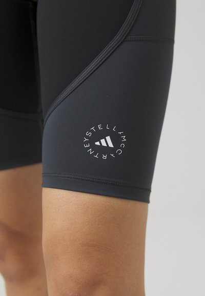 Black athletic shorts made of stretchy fabric, featuring a close fit. Notable white circular logo near the hem, with geometric accents.