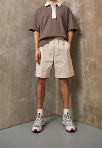 Šedý polo tričko s krátkým rukávem a bílým límečkem; světlé béžové cargo šortky s bočními kapsami; bílé tenisky s šedými a červenými akcenty.