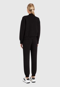 Felpa nera e pantaloni sportivi realizzati in tessuto morbido, con polsini e vita a costine. Abbinati a scarpe bianche con accenti neri.