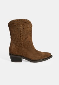 Braune Wildleder-Cowboy-Stiefel mit runder Zehe, dekorativen Ausschnitten und gesteppten Akzenten an der Oberseite. Sie haben einen niedrigen Absatz und eine glatte Sohle.