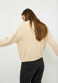 Beige, oversized knit sweater with long sleeves, ribbed hem. Worn with black jeans, showcasing a relaxed fit and soft texture.