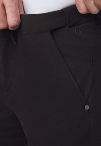 Czarne materiałowe spodnie o gładkiej fakturze, ukośne kieszenie i widoczny, markowy guzik na pasie.