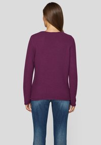 Violetter gestrickter Pullover mit einem strukturierten Muster, Rundhalsausschnitt und langen Ärmeln, kombiniert mit blauen Jeans. Ansichtsseite zeigt die Rückseite.