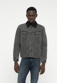 Jachetă din denim gri cu guler din blană artificială neagră, buzunare frontale și închidere cu nasturi. Mâneci lungi, croială ușor supradimensionată, detalii cu cusături liniar.