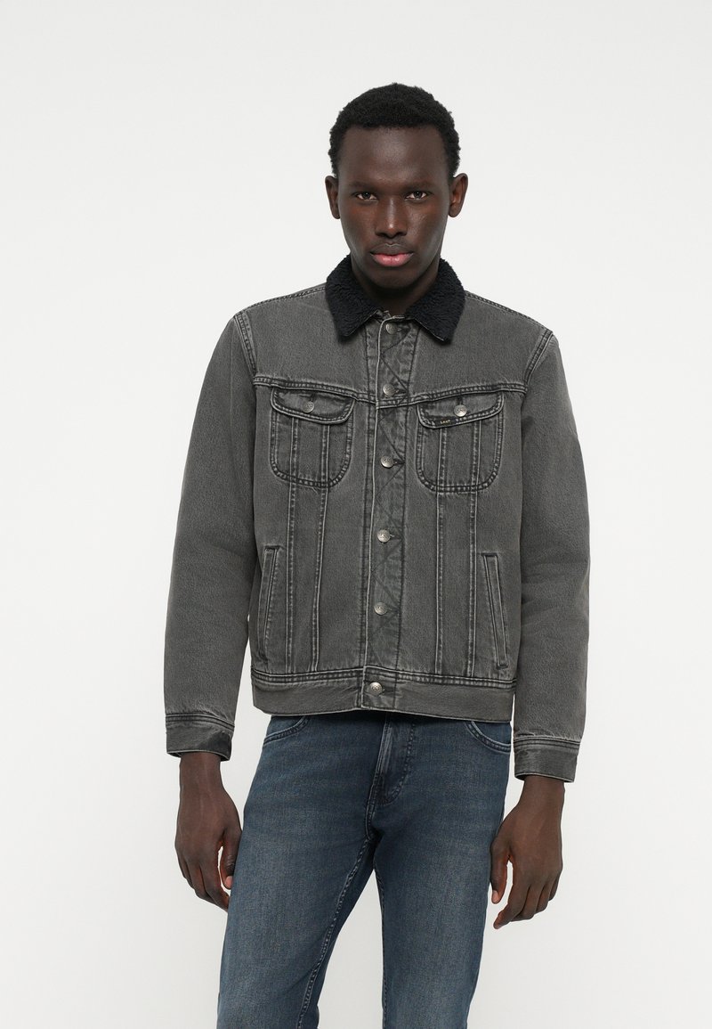 Jachetă din denim gri cu guler din blană artificială neagră, buzunare frontale și închidere cu nasturi. Mâneci lungi, croială ușor supradimensionată, detalii cu cusături liniar.