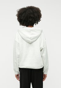 Γκρίζα φ�όρμα με άνετη εφαρμογή, διαθέτει μεγάλη κουκούλα και ρίγες στους ώμους. Μαλακή υφή και ριμπ μανσέτες. Μαύρο παντελόνι μερικώς ορατό.