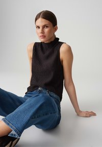 Black sleeveless top with a textured finish, paired with light blue oversized jeans, viewed from a seated position.