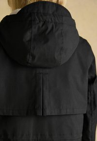 Schwarze Kapuzenjacke aus strukturiertem Material, mit geschichteten Design und Rückenbelüftung, sichtbaren Nähten und sauberem Finish.