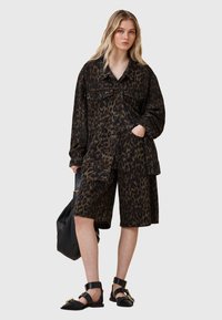 Ensemble composé d'une veste et d'un short à imprimé léopard, dans des tons noirs et bruns, fabriqu�é en toile, avec des poches avant et des fermetures à bouton. Sac à main noir et sandales.
