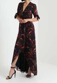 Maxi šaty v černé barvě s květinovým vzorem v odstínech červené a zelené, s krátkými rukávy se mašlemi a bočním rozparkem. Vyrobeno z lehké látky.