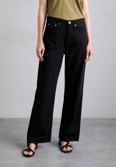 Black wide-leg jeans made of cotton with a smooth texture, featuring front pockets, silver hardware, and a high waist. Paired with black sandals.