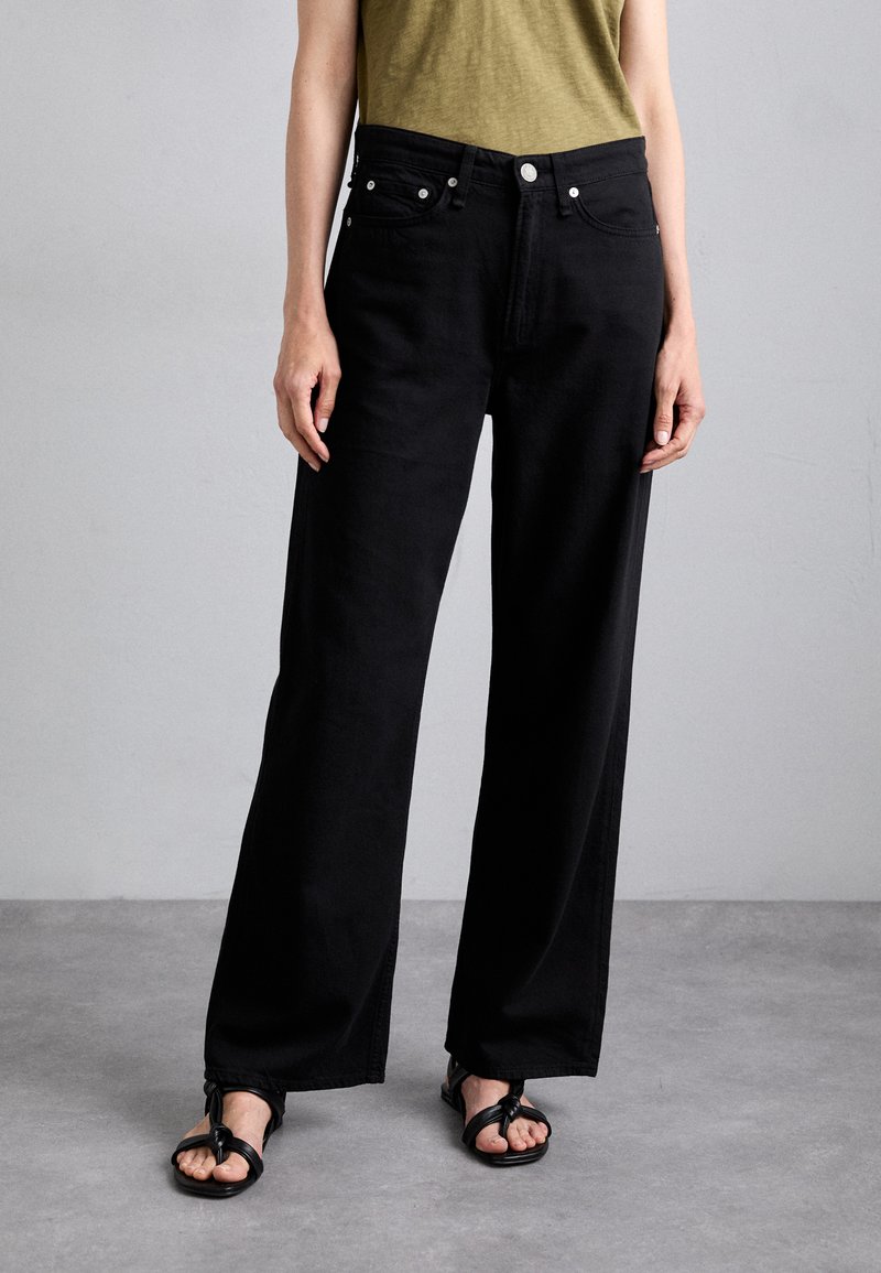 Black wide-leg jeans made of cotton with a smooth texture, featuring front pockets, silver hardware, and a high waist. Paired with black sandals.