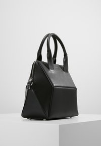 Czarna skórzana torebka z geometrycznym wzorem, z krótkimi uchwytami, zamkiem błyskawicznym i srebrną metką. Gładka tekstura i wyraźny kształt.