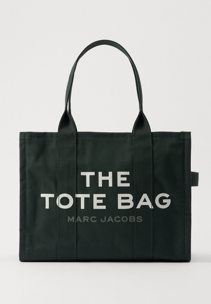 Zwarte canvas draagtas met twee handvaten, bedrukt met vet witte tekst "THE TOTE BAG" en kleinere grijze tekst "MARC JACOBS" aan de voorkant.