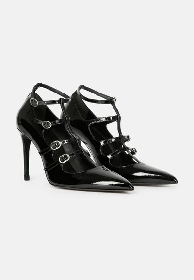 Chaussures à talons hauts en cuir verni noir, bouts pointus, design à bride en T et cinq boucles argentées réglables sur chaque chaussure.