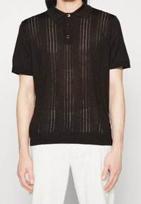Hnědá polo tričko s krátkým rukávem a texturovaným pleteným vzorem, s límečkem a třemi tmavými knoflíky vepředu.