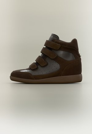 Brązowy wysokiej cholewce sneaker z trzema szerokimi paskami na rzepy i perforowanymi panelami ze skóry na gładkim beżowym tle.
