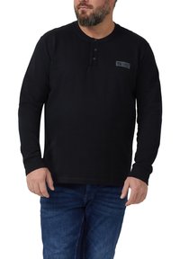 Czarna koszula z długim rękawem z dekoltem henley z trzema guzikami. Materiał jest gładki z subtelna elastycznością. Noszona z niebieskimi dżinsami.