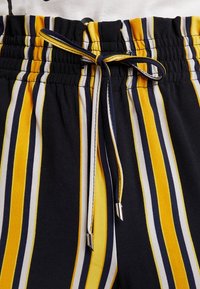 Randiga byxor i marinblått, gult och vitt tyg. Har en elastisk midja med dragsko och silverfärgade stoppare. Mjuk textur.
