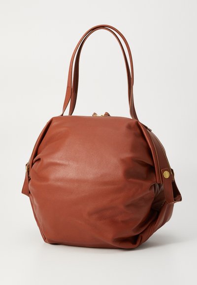 Brown leather handbag with a rounded shape, double handles, and zip closure. Features soft texture and subtle gold hardware accents.