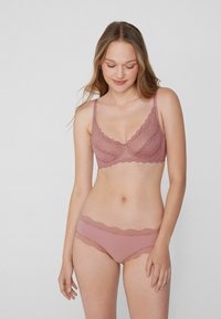 Krajková podprsenka a odpovídající kalhotky v jemném růžovém odstínu. Podprsenka má zvlněné okraje, nastavitelné ramínka a květinové krajkové detaily.