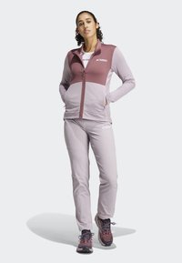 Terrex aktivna odjeća koja uključuje jaknu s patentnim zatvaračem u boji mauve i odgovarajući par laganih, rastezljivih hlača.