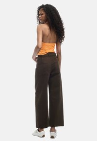 Top ajustado naranja, pantalones de tiro alto marrones de pierna ancha y zapatillas blancas. El conjunto presenta una parte superior texturada y unos pantalones amplios y holgados.