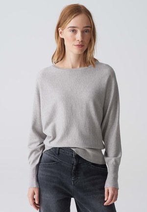 Lichtgrijze langslavertop met een brede halslijn en een relaxte pasvorm, gecombineerd met donkere jeans. Zachte textuur en minimale ontwerpdetaillering.