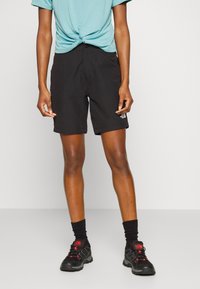 Svarta shorts i ett lätt material, med fickor i midjan och en liten märkesetikett. I kombination med en knuten blå t-shirt och svarta vandringsskor.