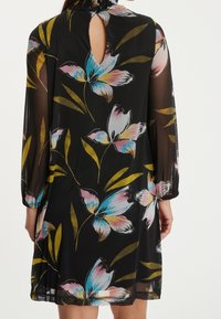 Vestido negro con flores, de manga larga transparente, con patrones de flores coloridos en rosa y azul, y detalle de abertura en la espalda con cierre de botón.