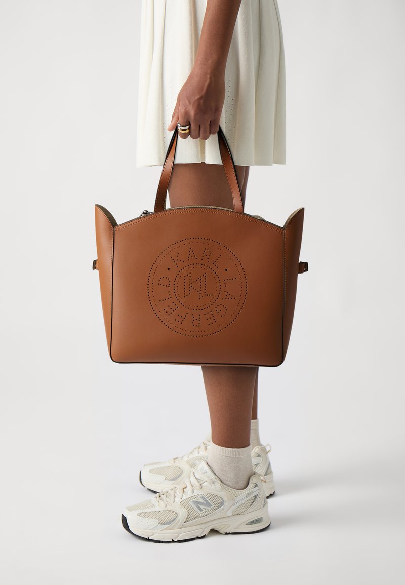 Borsa in pelle marrone chiaro con dettagli a logo perforato, forma strutturata, doppio manico, texture liscia e zip a contrasti.