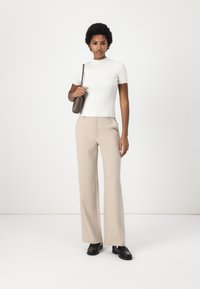 White ribbed short-sleeve top, beige wide-leg trousers, black shoes. Model holds a brown shoulder bag. Plain background.