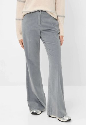 Pantalons en velours côtelé gris évasés avec une texture lisse, des poches avant et un bouton de fermeture. Portés avec des baskets argentées.