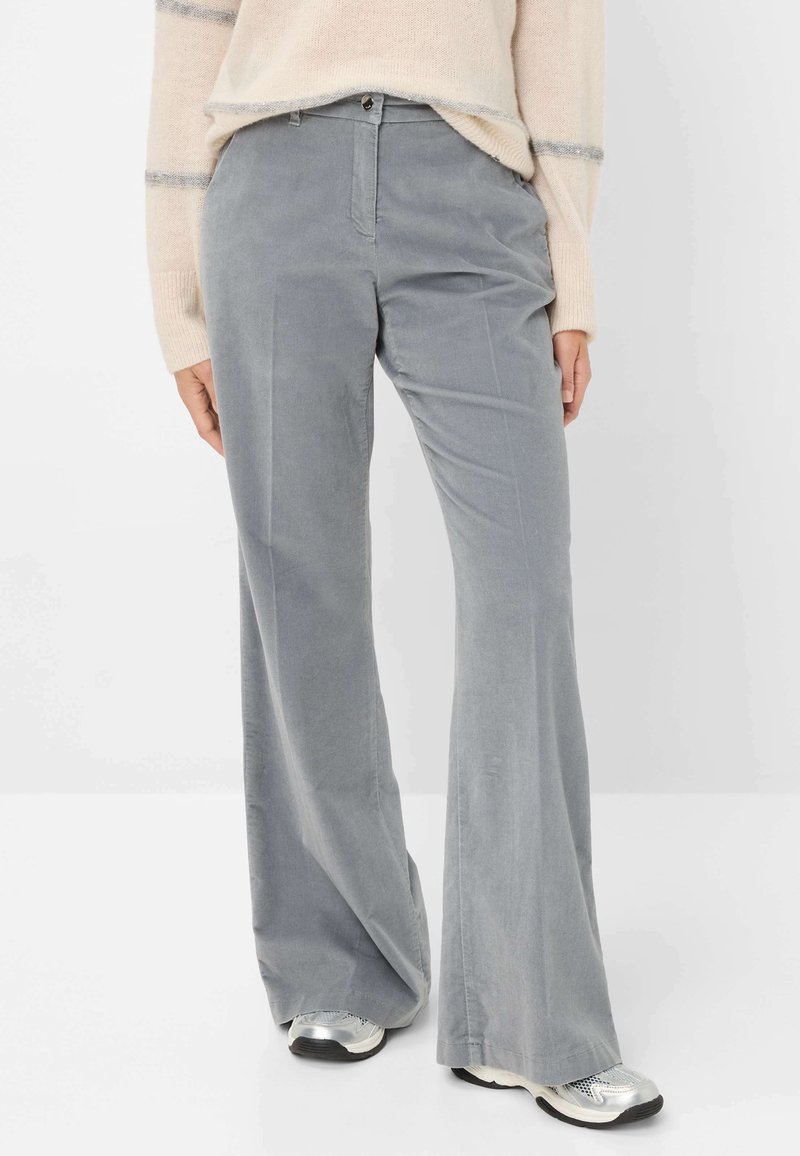 Grijze fluwelen flared broek met een soepele textuur, voorzakken en een knoopsluiting. Gecombineerd met zilveren sneakers.