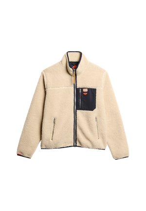 Beige fleecetrui met marineblauwe accenten, hoge kraag, twee ritszakken aan de zijkanten en een borstzak. Heeft een rubberen logo-opdruk op de borst.