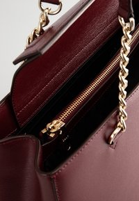 Sac à main en cuir bordeaux ouvert avec des anses en chaîne dorée montrant un compartiment intérieur zippé et des emplacements pour cartes.