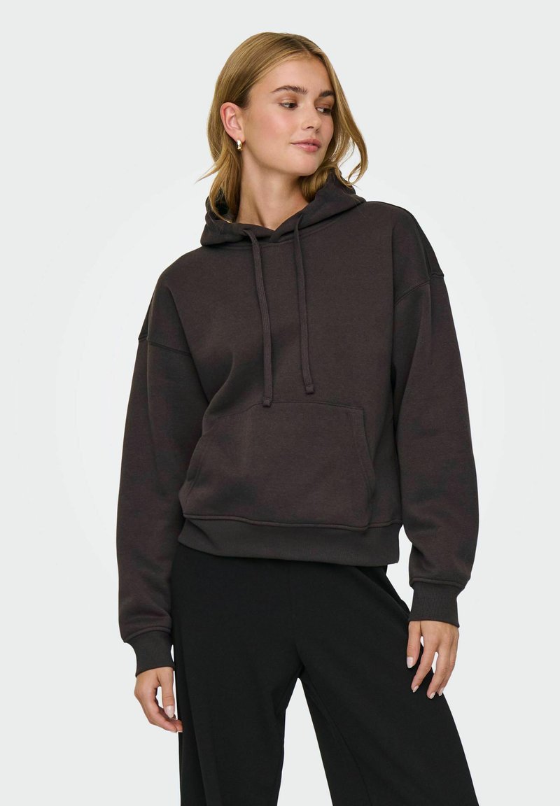Donkerbruin hoodie van zachte stof, voorzien van een voorzak, verstelbare trekkoordjes en ribbed cuffs en zoom. Gepaard met zwarte broek.