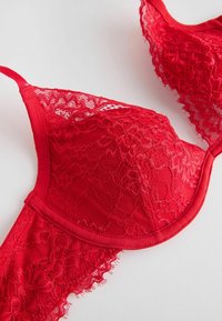 Red lace bra featuring a textured floral pattern, molded cups, and adjustable straps, with a smooth fabric band and lace trim accents.
