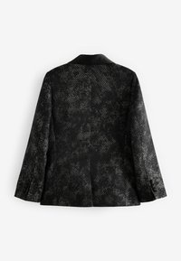 Svart mönstrad kavaj i en texturerad tyg, med kontrasterande satinrevers och knäppta manschetter. Bakifrån visar den en strukturerad silhuett och detaljer.
